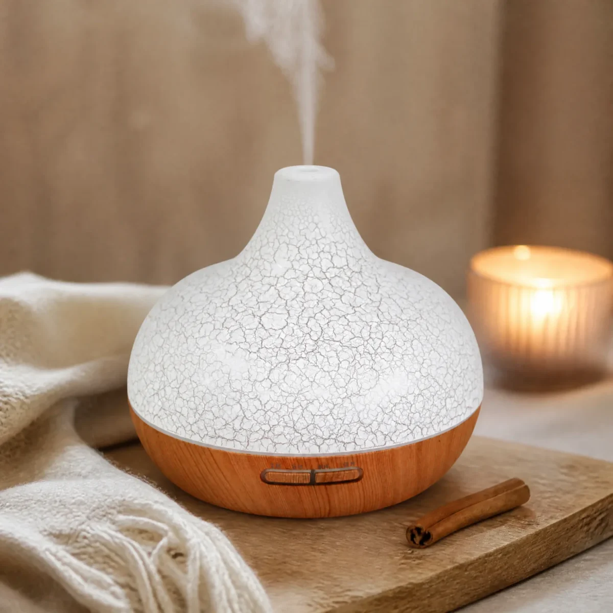 Aroma diffuser Santorini met craquelé-effect en een houtlook voet, met damp, naast een kaneelstokje, een kaars en een wollen plaid