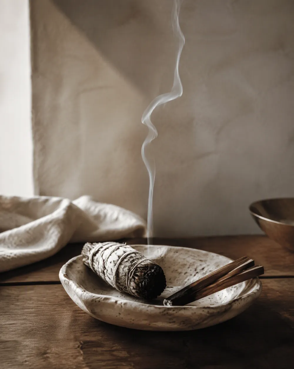 Bundel witte salie en palo santo in een keramisch schaaltje met een sliert rook