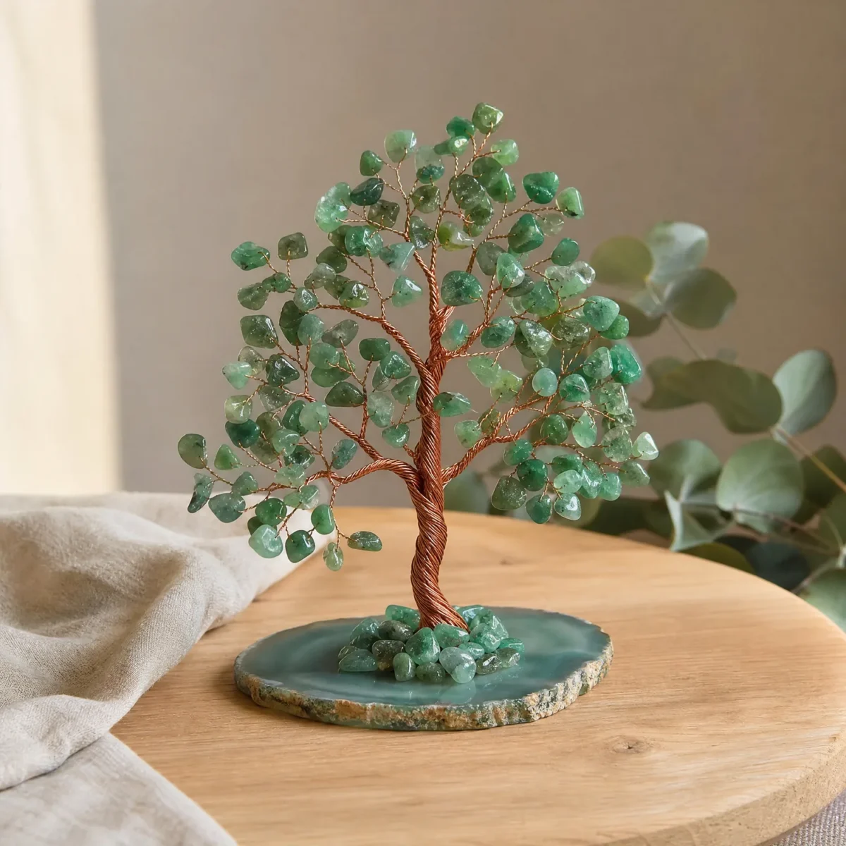 Groot edelsteenboompje met groene aventurijn op een schijf van groene agaat, op een eikenhouten plank naast linnen en eucalyptus