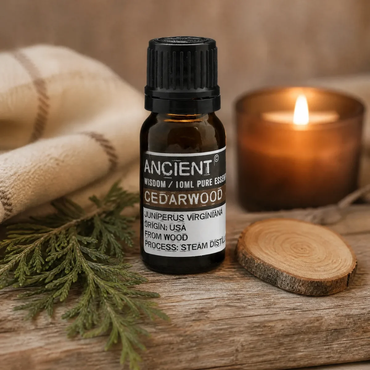 Flesje etherische olie cederhout van 10 ml naast een brandende kaars, een cederhouttakje en een houten schijfje