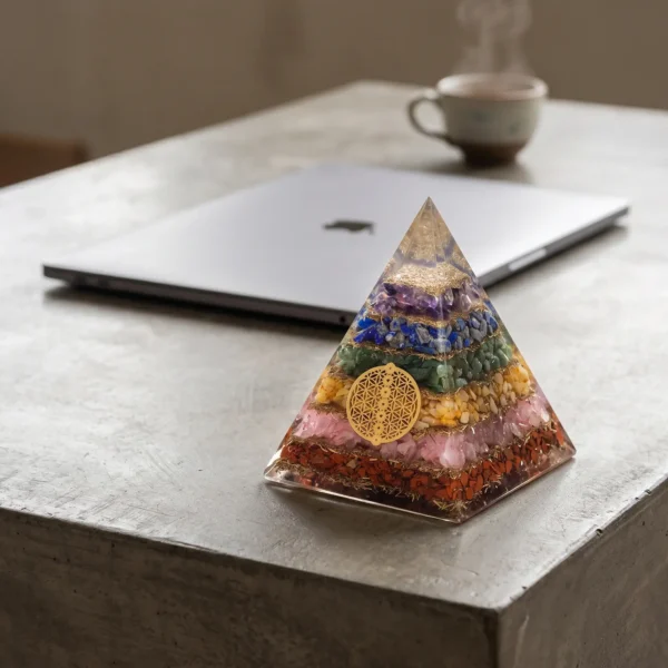 Orgoniet piramide in chakrakleuren naast een laptop op een betonnen tafel